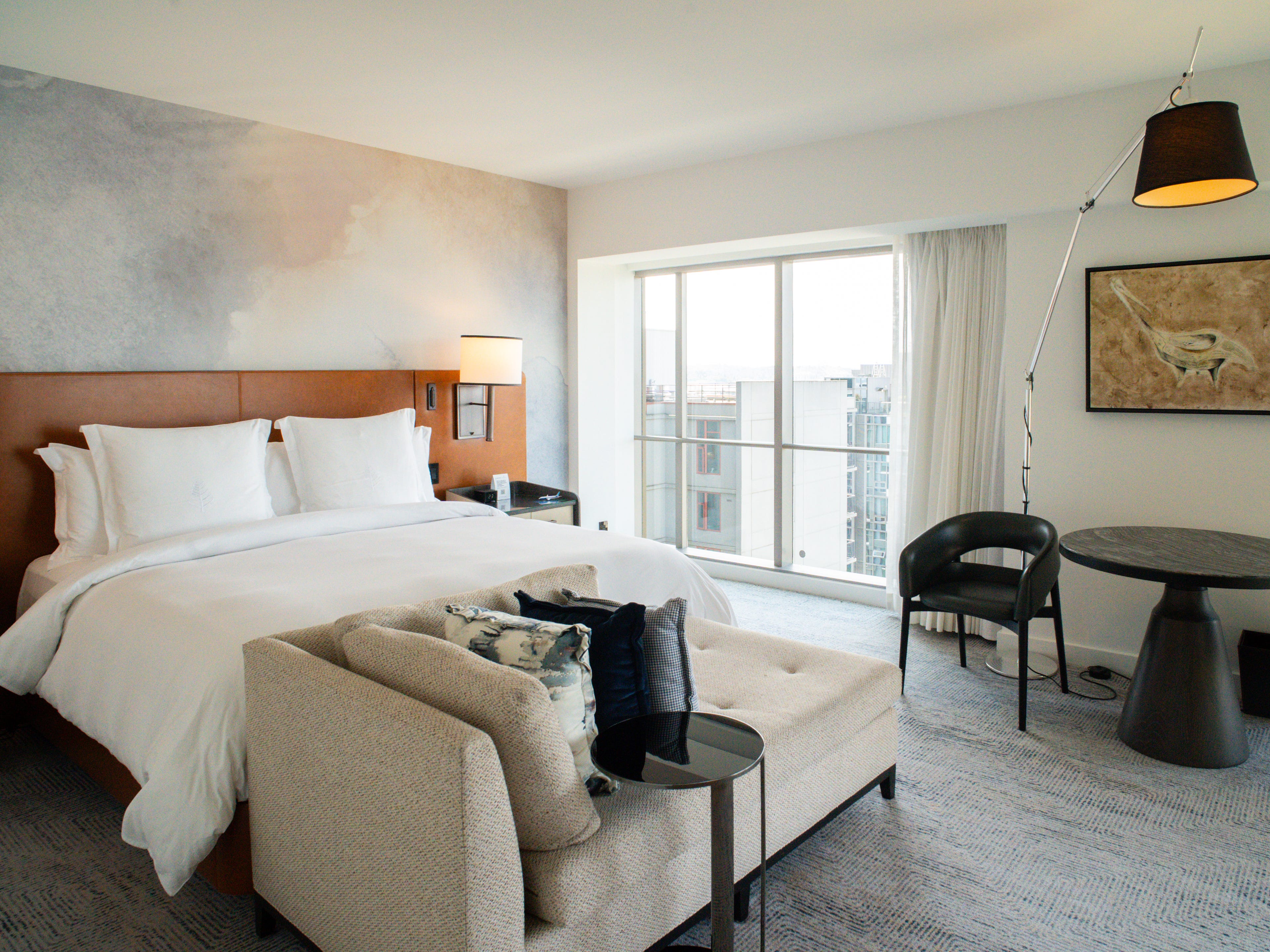 Inside a suite at the Four Seasons Seattle with a bed on the left, a table on the right, and a window in the back