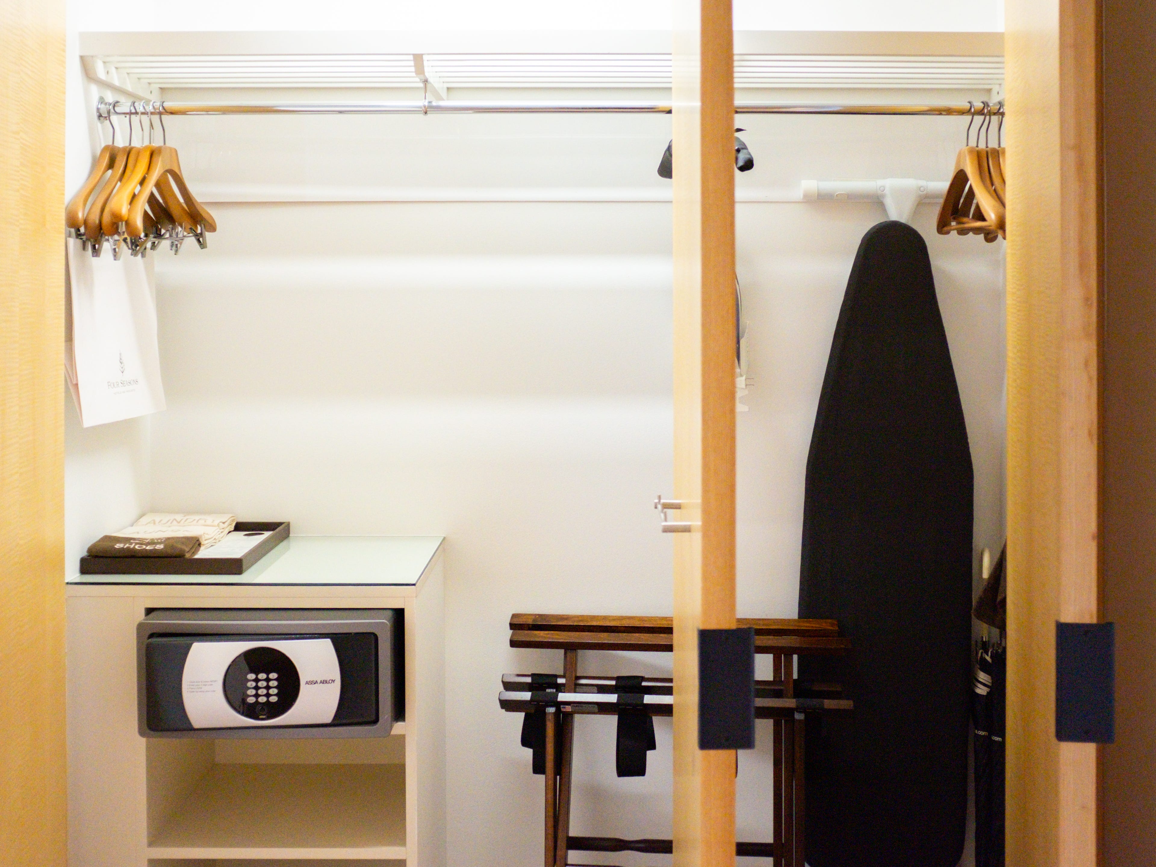 Inside a Four Seasons Seattle hotel room, there's a closet with an ironing board, hangers, luggage racks, umbrellas, shelves, and a safe