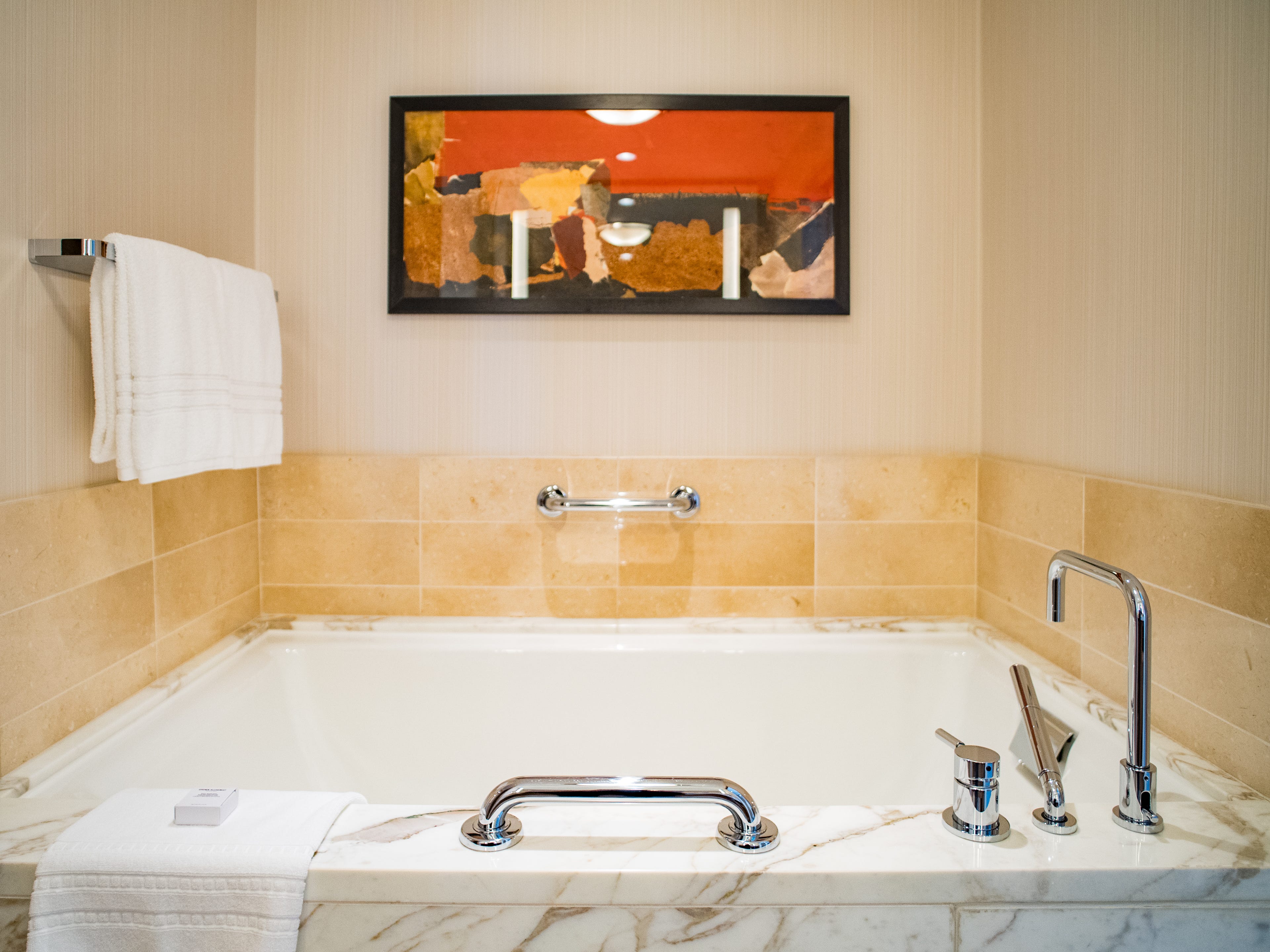 Inside a Four Seasons Seattle hotel bathroom, there's a marble tub with a framed picture on the wall above