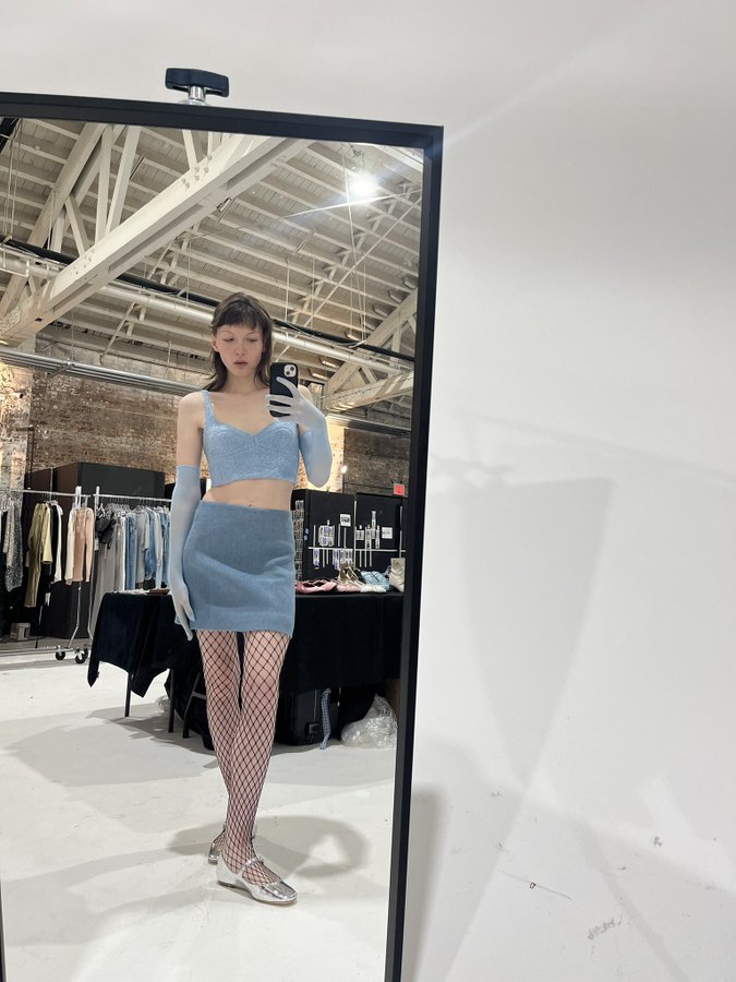Miles Yardley in light blue crop top and skirt taking a selfie in a mirror.