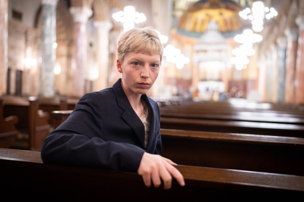 Portrait of Miles Yardley, a detransitioned model, sitting in a church pew.