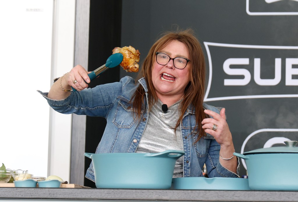 Rachael Ray holding up a piece of cooked chicken with tongs.