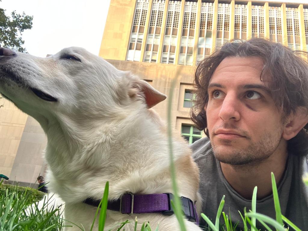 Sam Nahins, a Columbia grad student, lying in the grass with his dog.