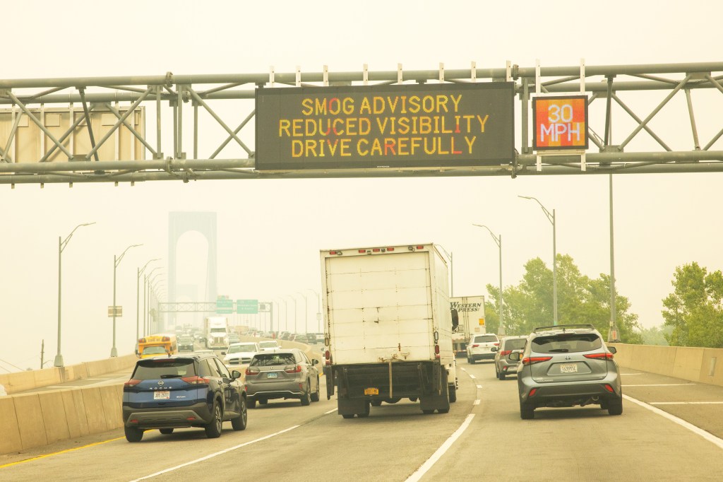 Smog advisory sign on a highway overpass; reduced visibility, drive carefully, 30 mph speed limit.