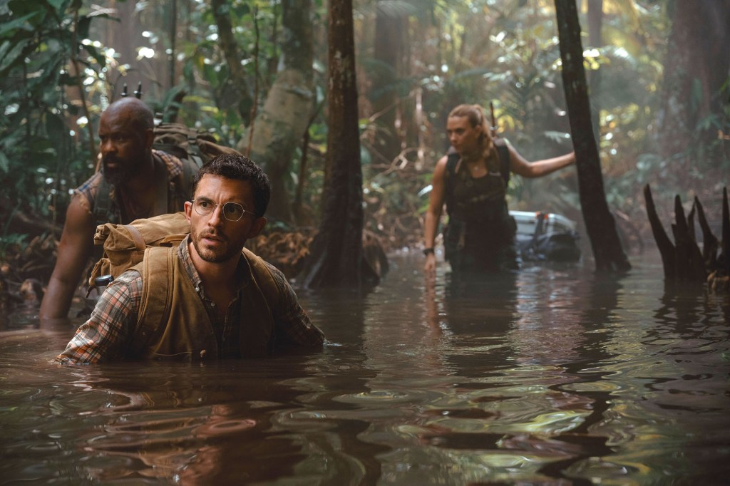 Still from Jurassic World: Rebirth showing Jonathan Bailey, Scarlett Johansson, and Bechir Sylvain wading through a swamp.