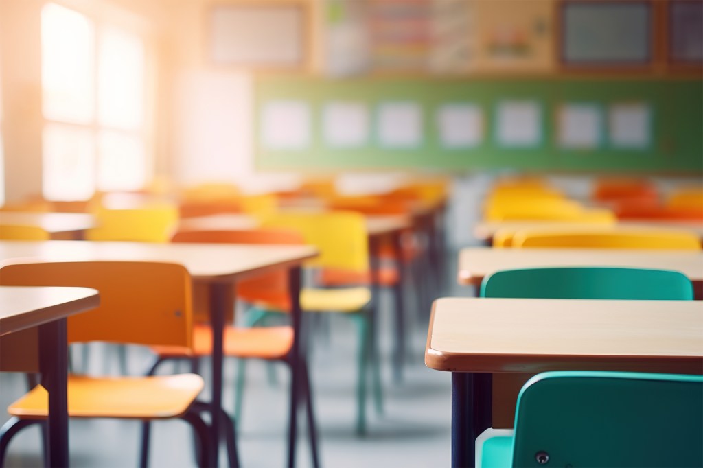 Blurred image of an empty school classroom with colorful desks and chairs.