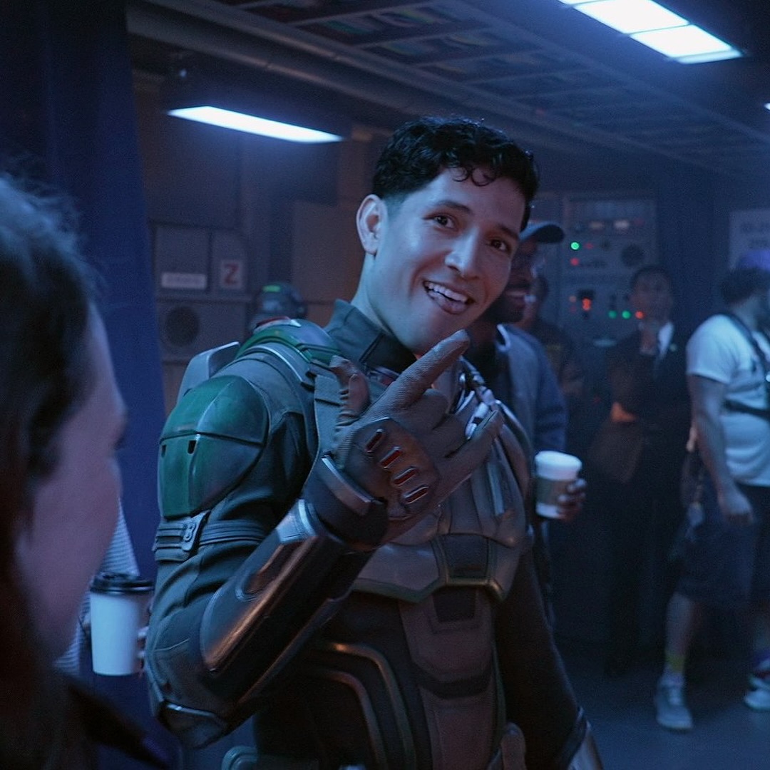 Danny Ramirez smiles on a movie set. 