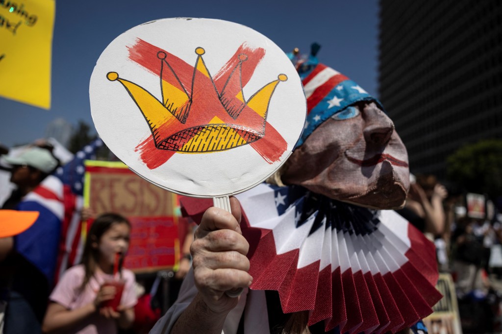 Protestor holding sign with crossed-out crown at immigration protest.