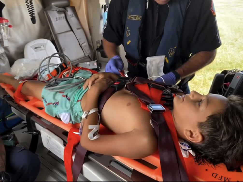 A young boy lies on a stretcher in an ambulance, receiving medical attention.