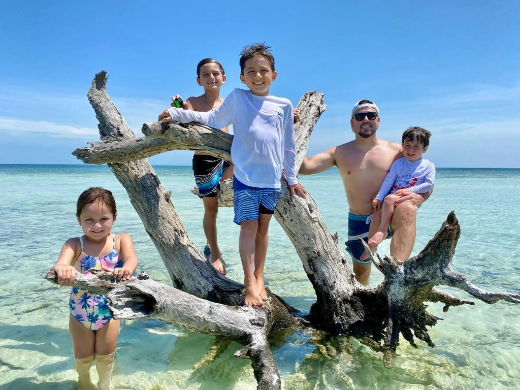 Family on a beach, standing on a partially submerged log.