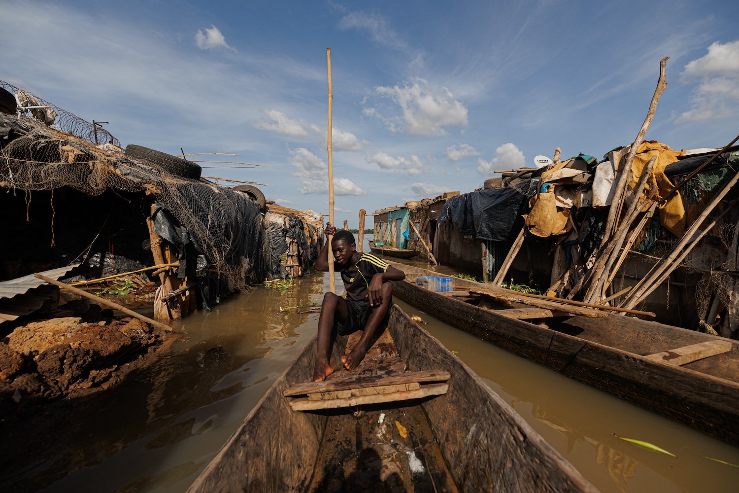 A boy sits in the middle of a long boat going through a submerged street.