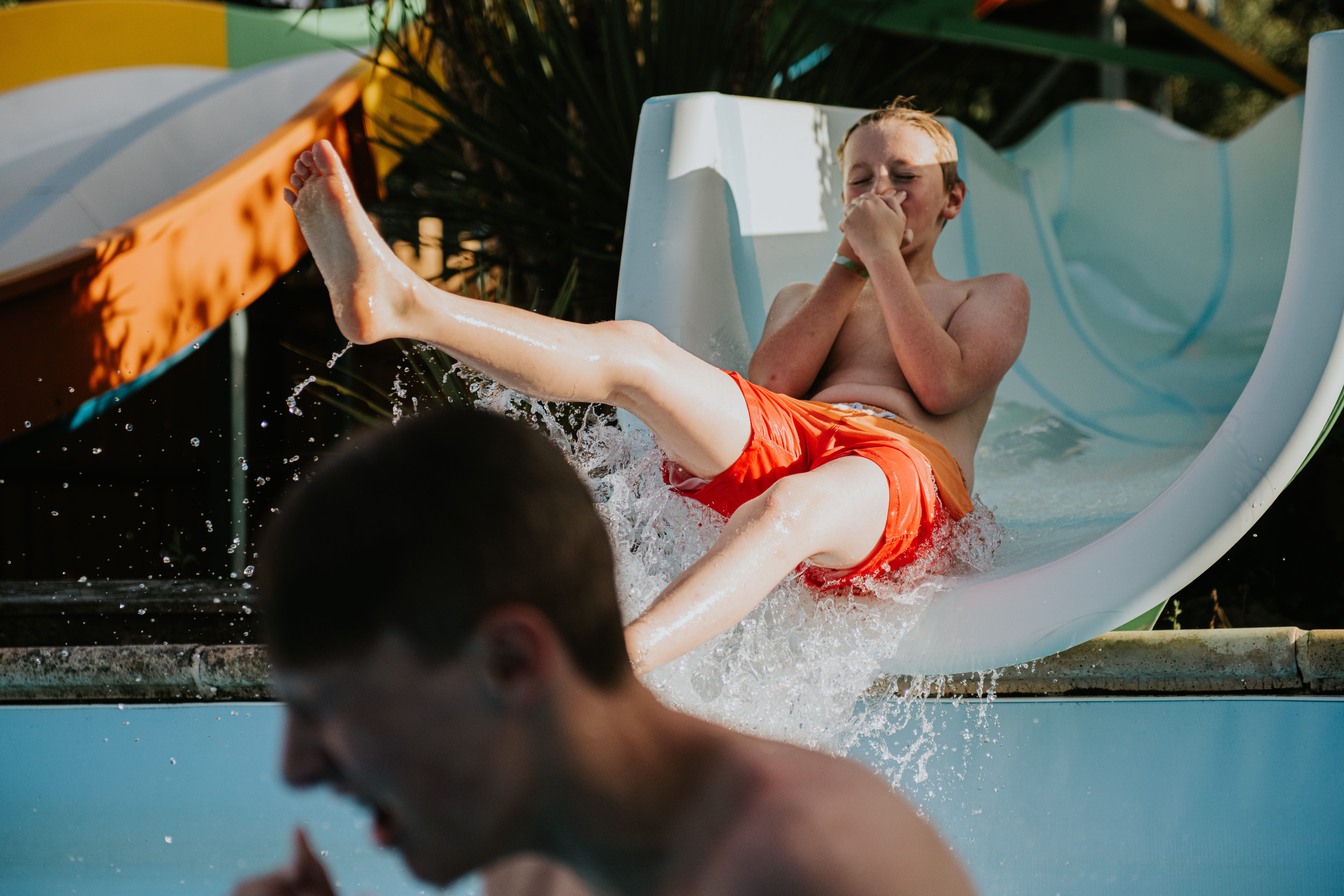 A young boy holds his nose as he braces for impact as he flies off the end of a waterslide in an amusement waterpark