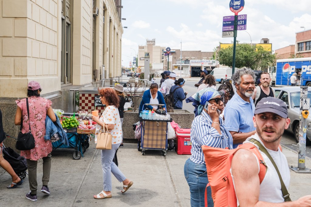 People selling fruit from carts on a city sidewalk.