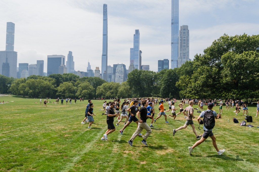 Large group of people running on a grassy field in front of a city skyline.