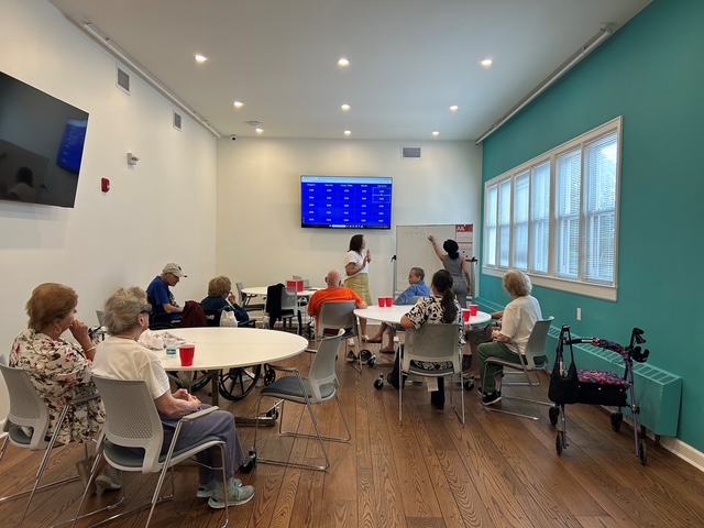 A group of seniors participates in a presentation in a room with a large screen and whiteboard.