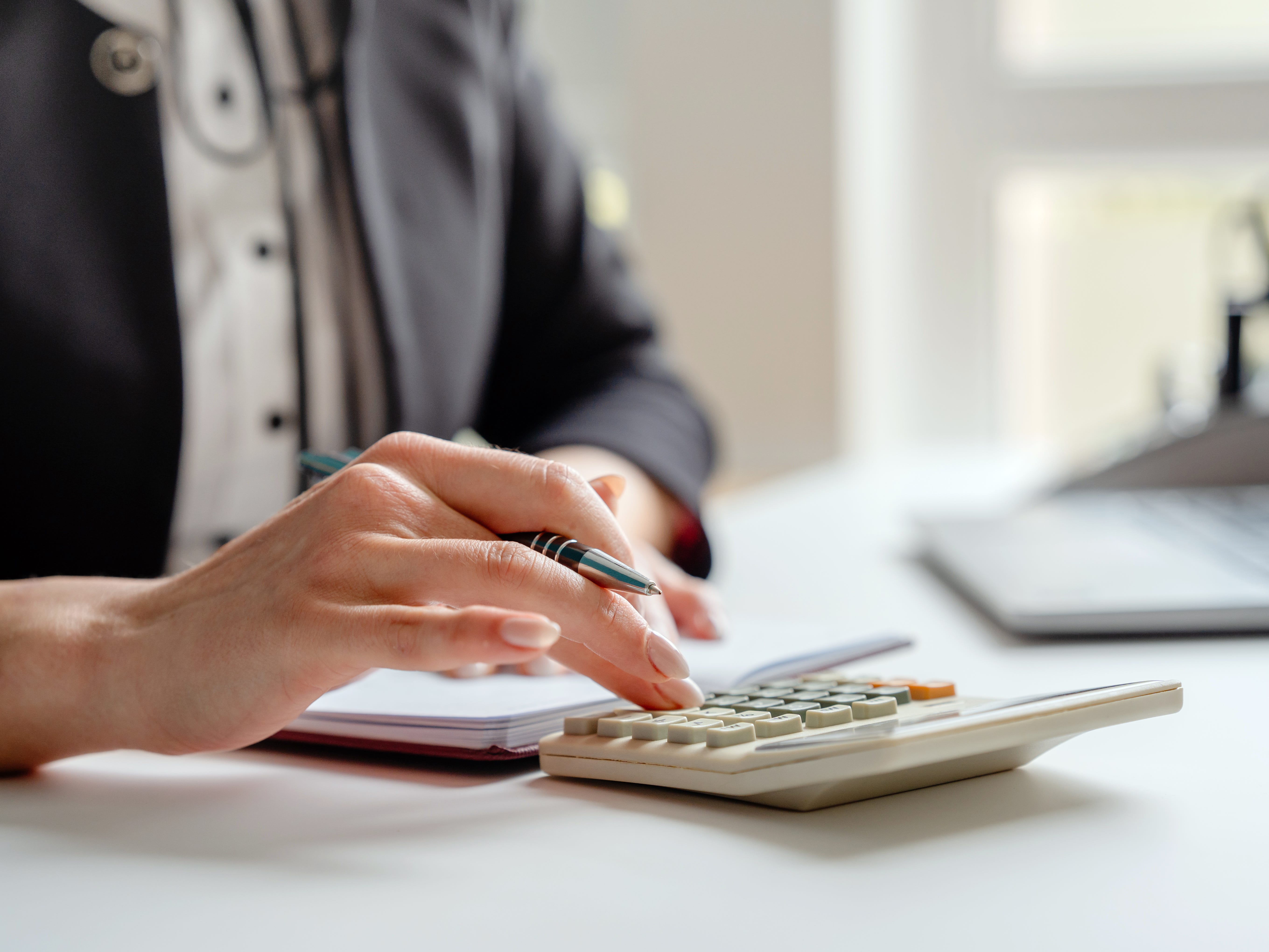 A woman types on a calculator while holding a pen and a notepad.