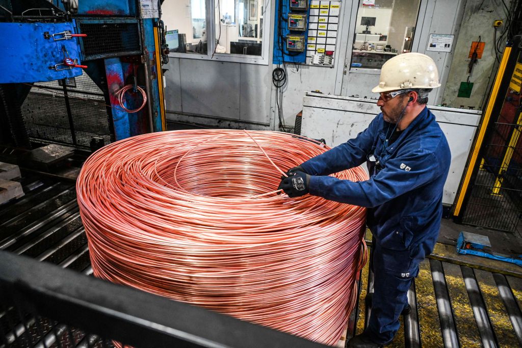 Worker handling a large spool of copper wire in a factory.
