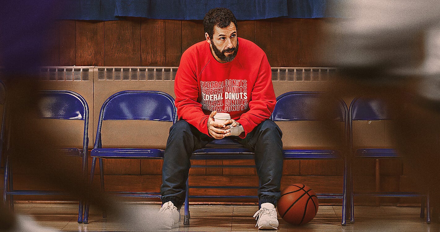 Adam Sandler sitting holding a coffee cup