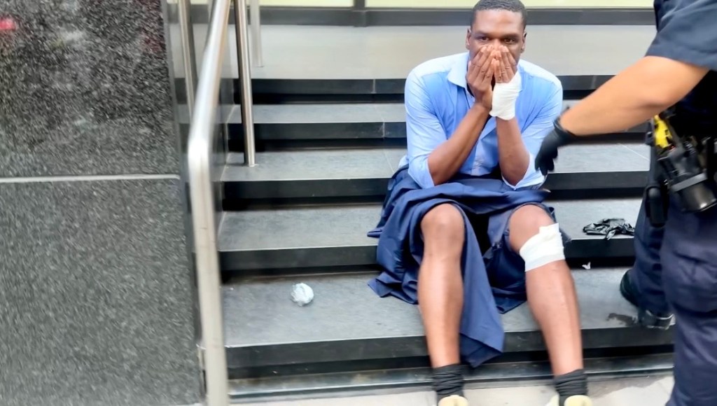 Injured man sitting on steps, police officer nearby.