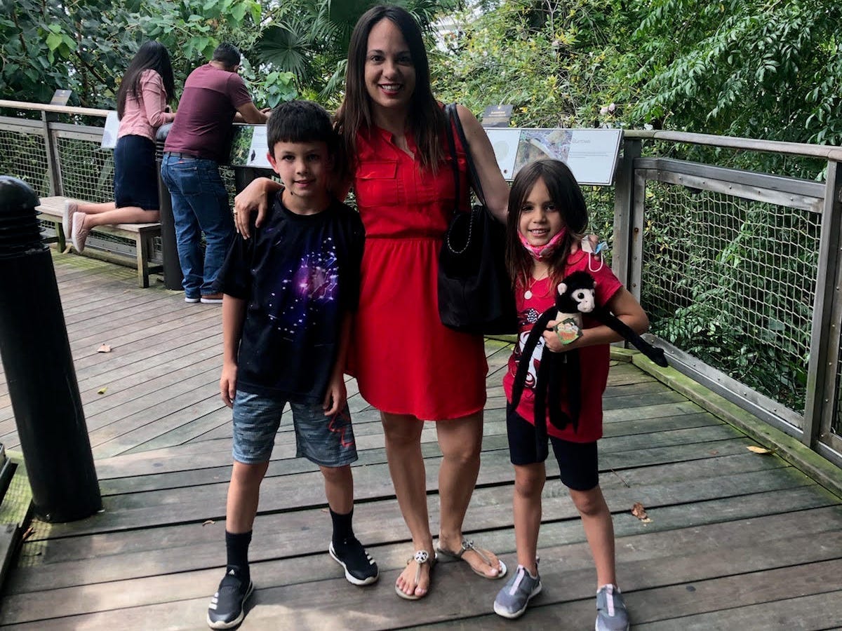 mother in red dress stands with her two kids outside