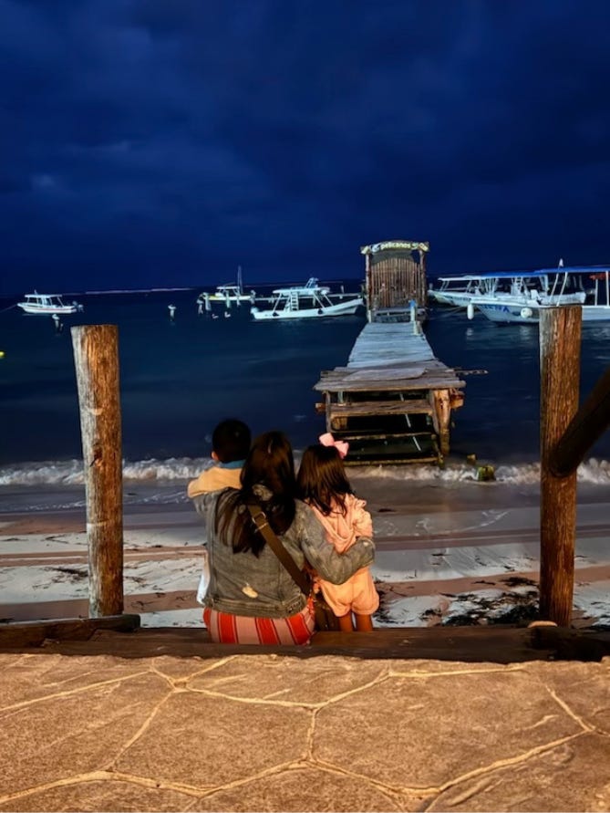 Ramos holding her two kids as they look out onto a body of water at some boats.
