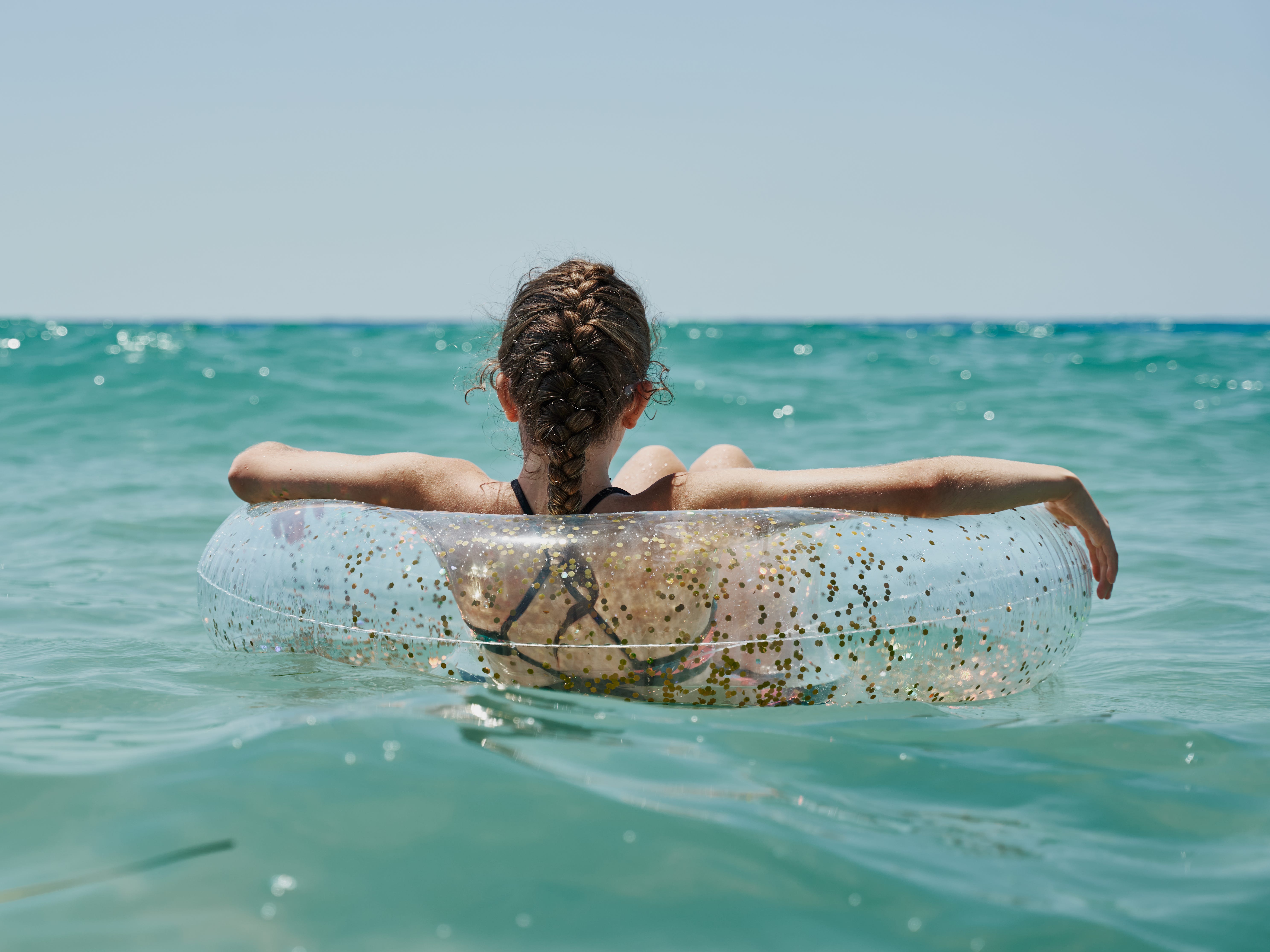 A girl with a braid facing away from the camera and floating on a tube in the ocean.