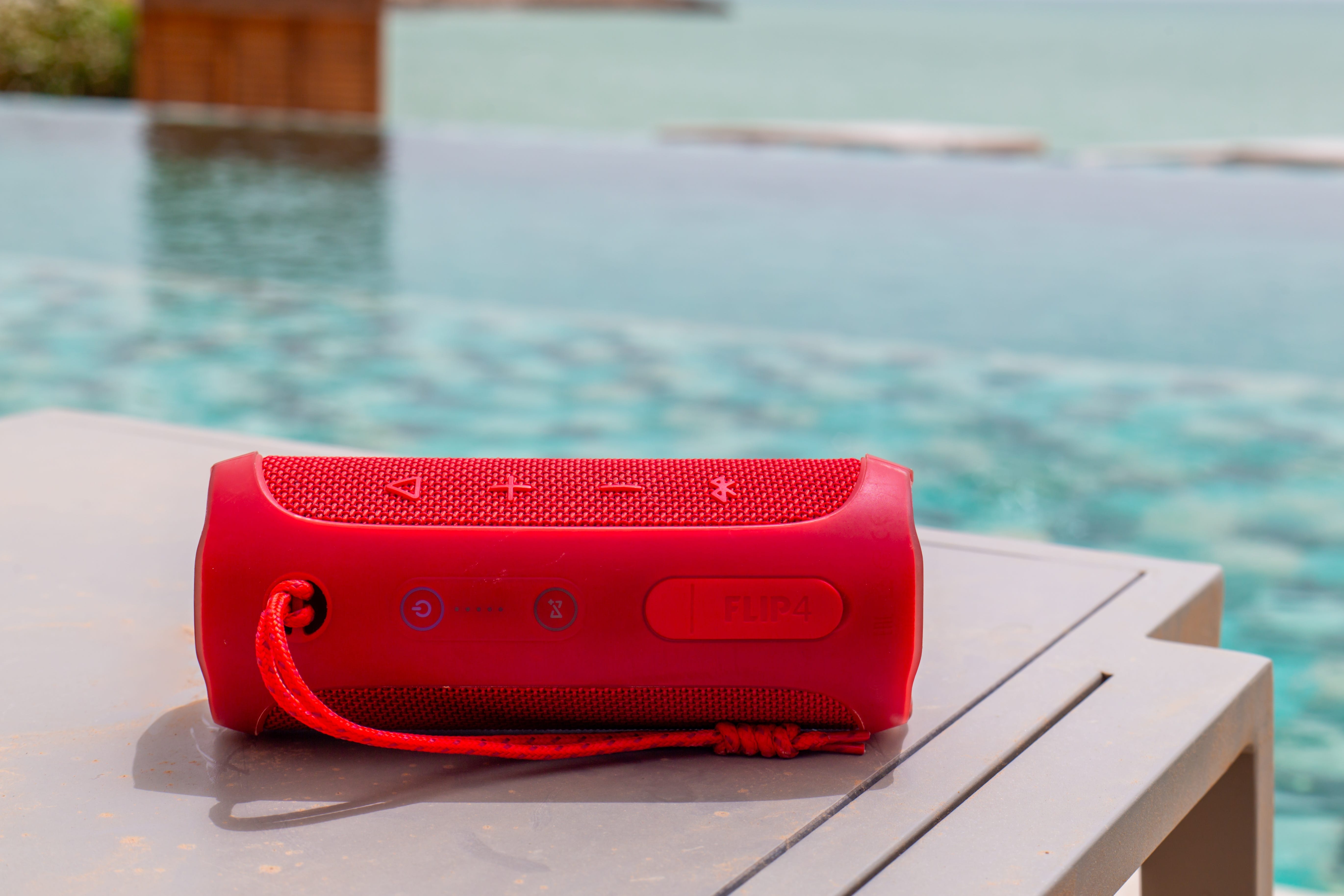 A red Bluetooth speaker on a poolside table.