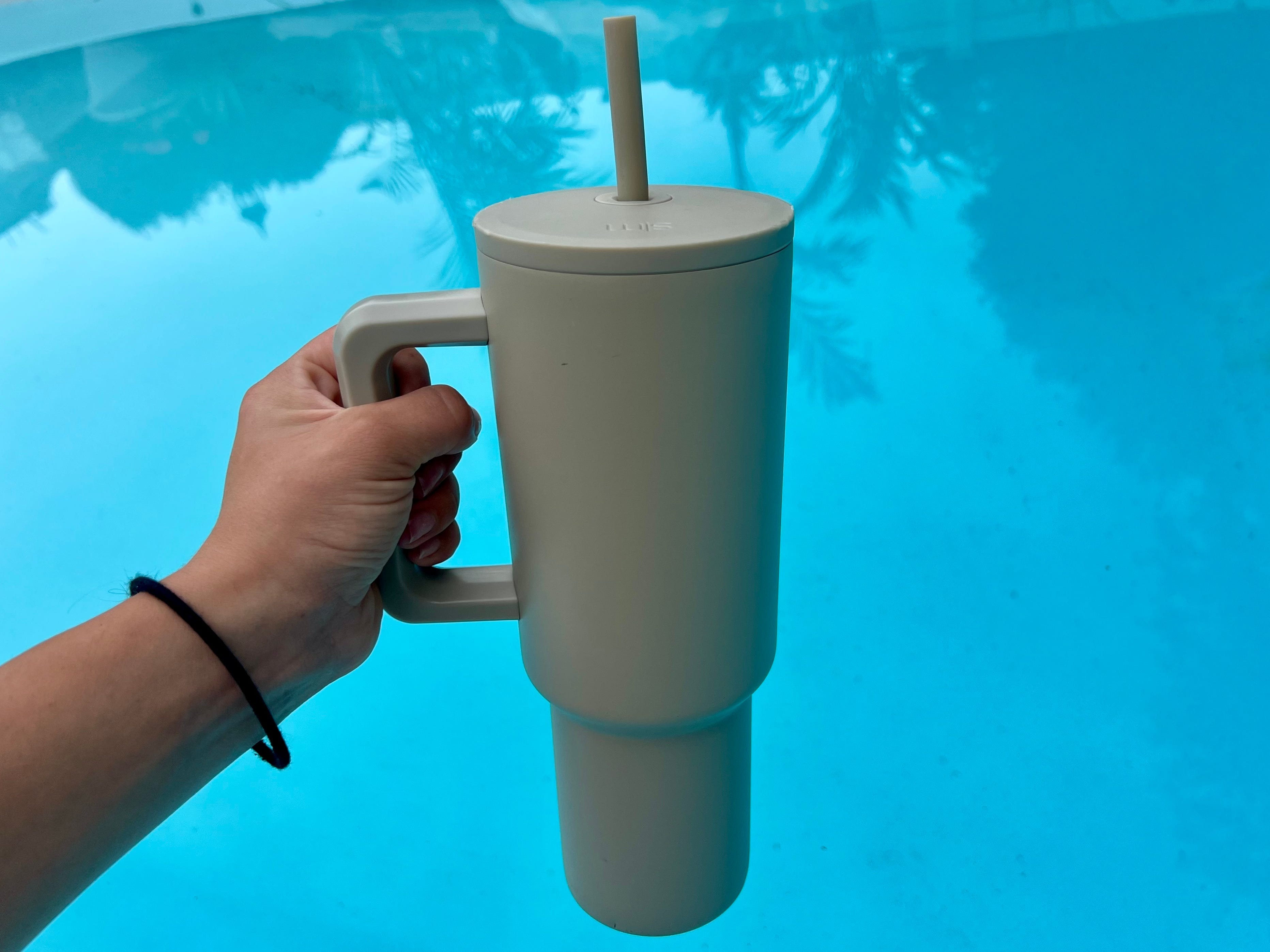 A hand holding a beige reusable water bottle over a body of water.