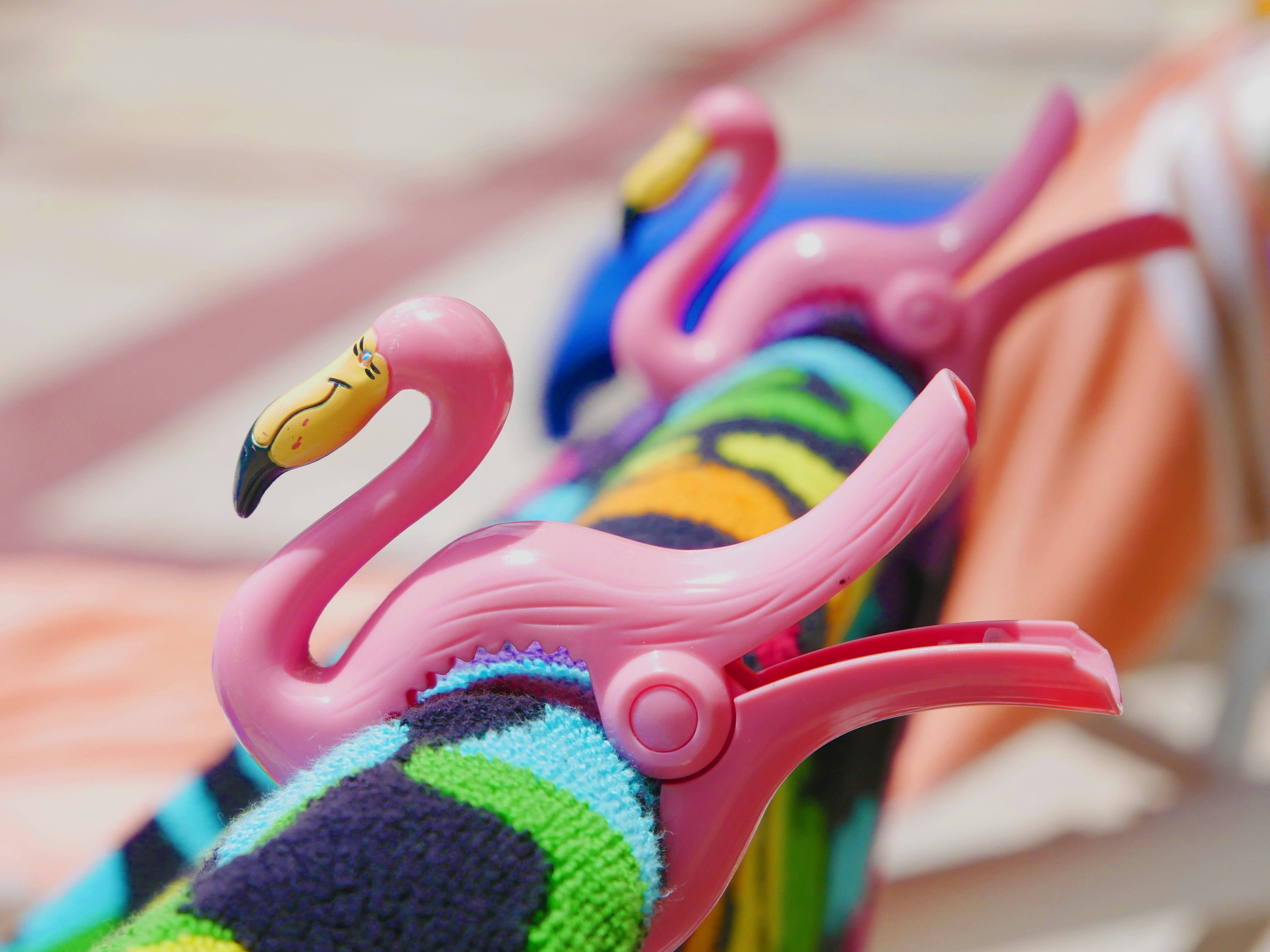 Flamingo-shaped towel clips holding a multicolored towel on a lounge chair.