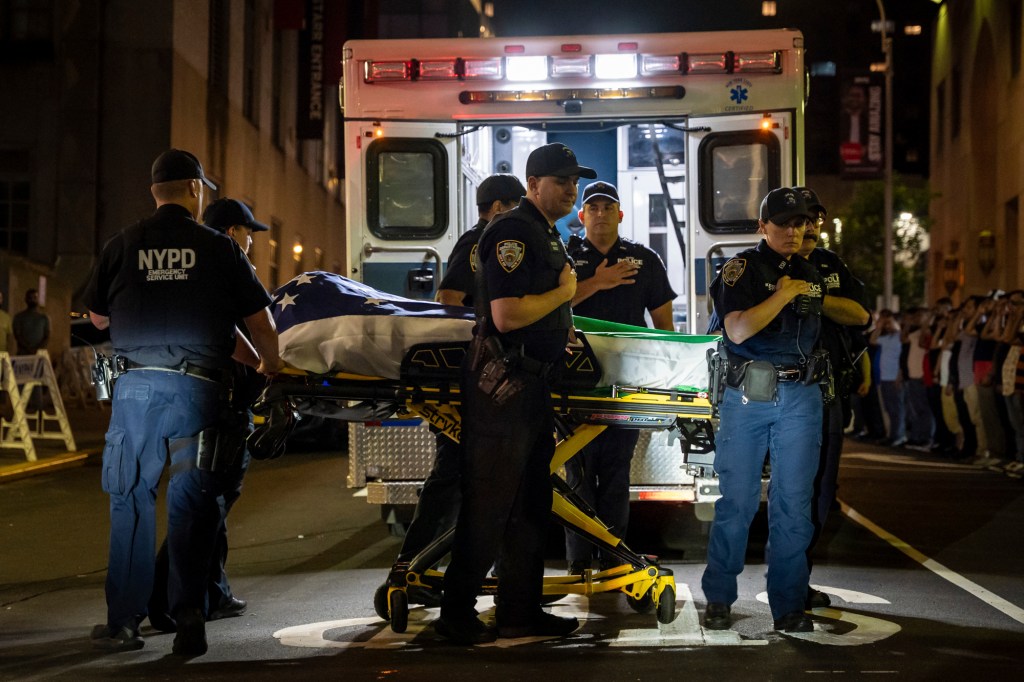 NYPD officers carry a body covered by an American flag from an ambulance.