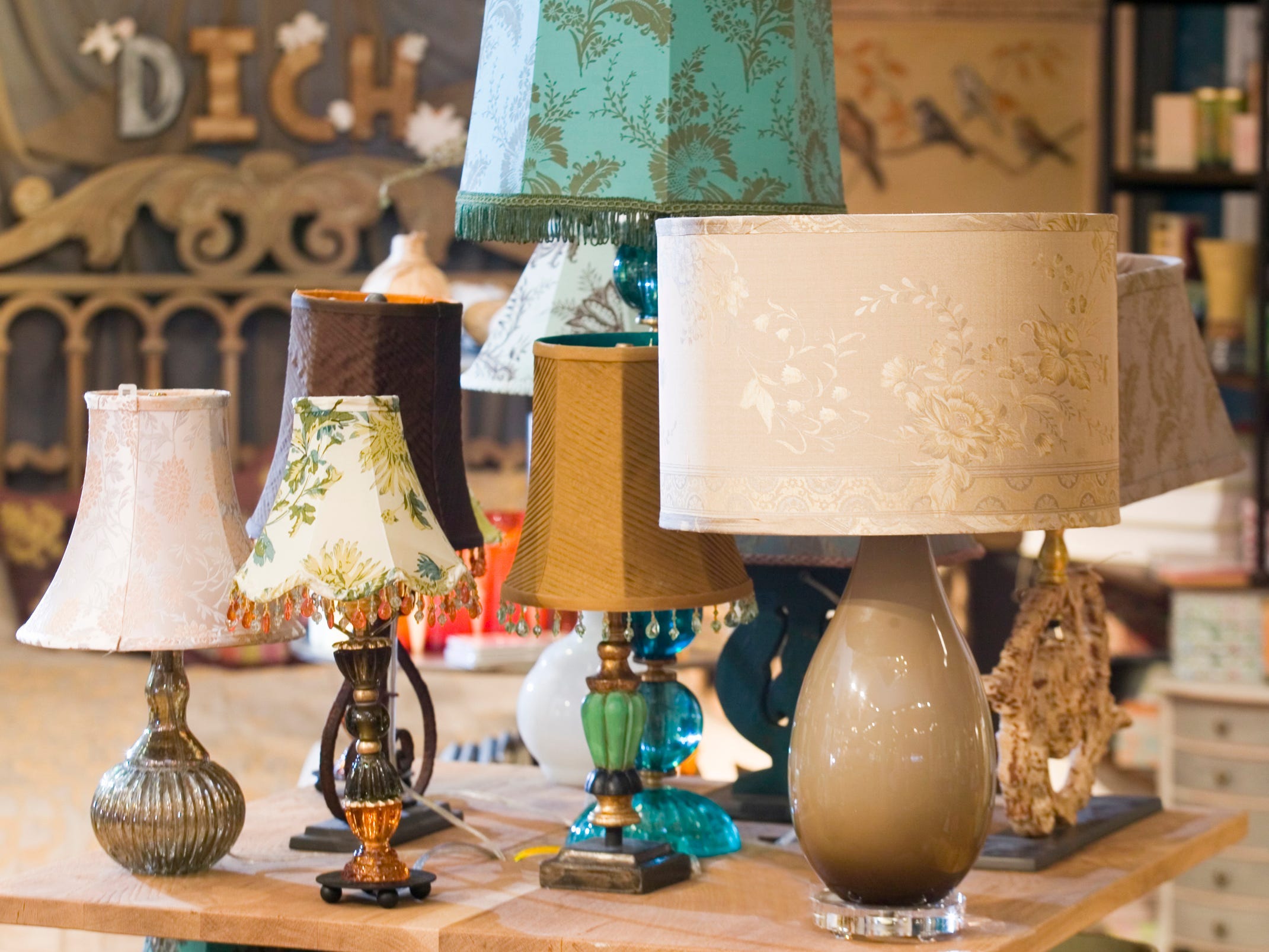 Several vintage-looking lamps on a wooden table at Anthropologie. Some lamps have beads hanging from the shades or shades with floral patterns