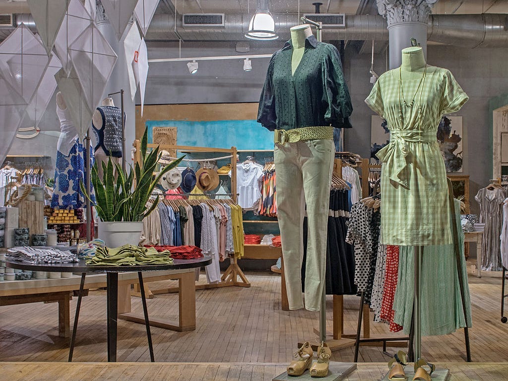 Two mannequins on display at Anthropologie. One mannequin wears a green shirt and pants and the other has a green gingham dress