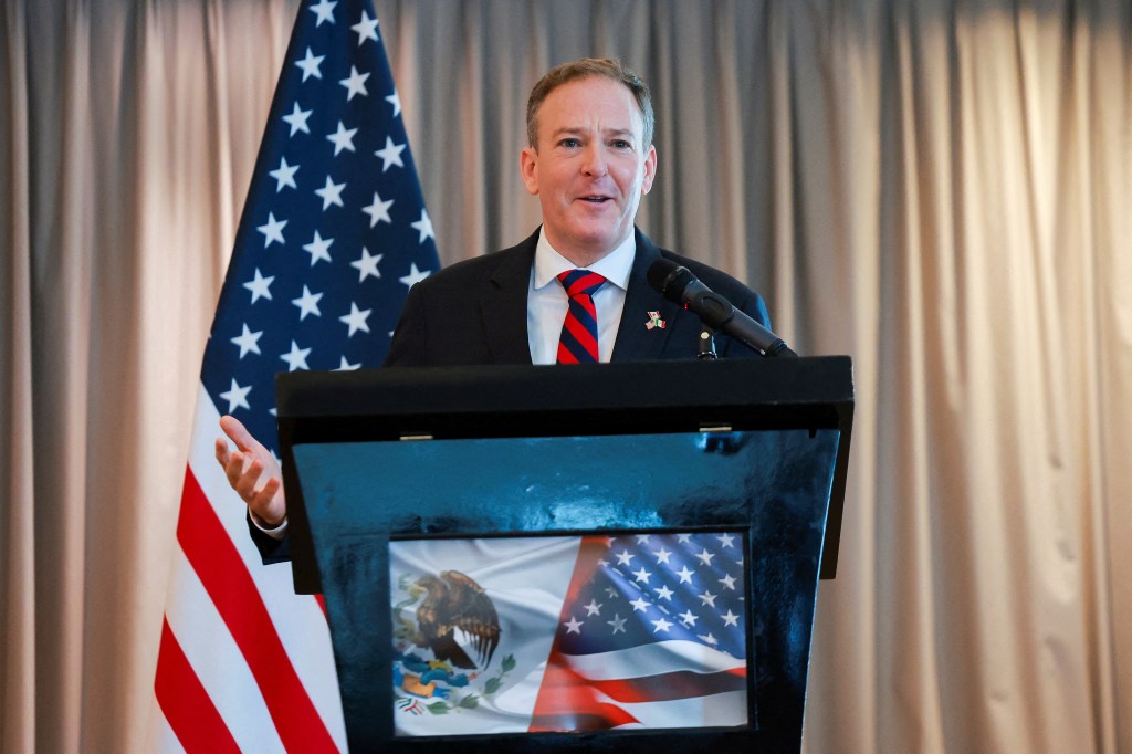 A man speaking at a podium; the US and Mexican flags are visible.