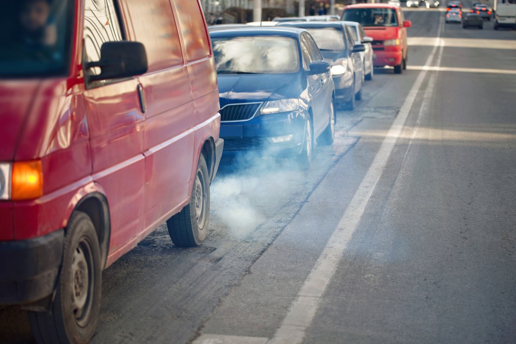 Exhaust smoke from a van in a line of stopped cars.