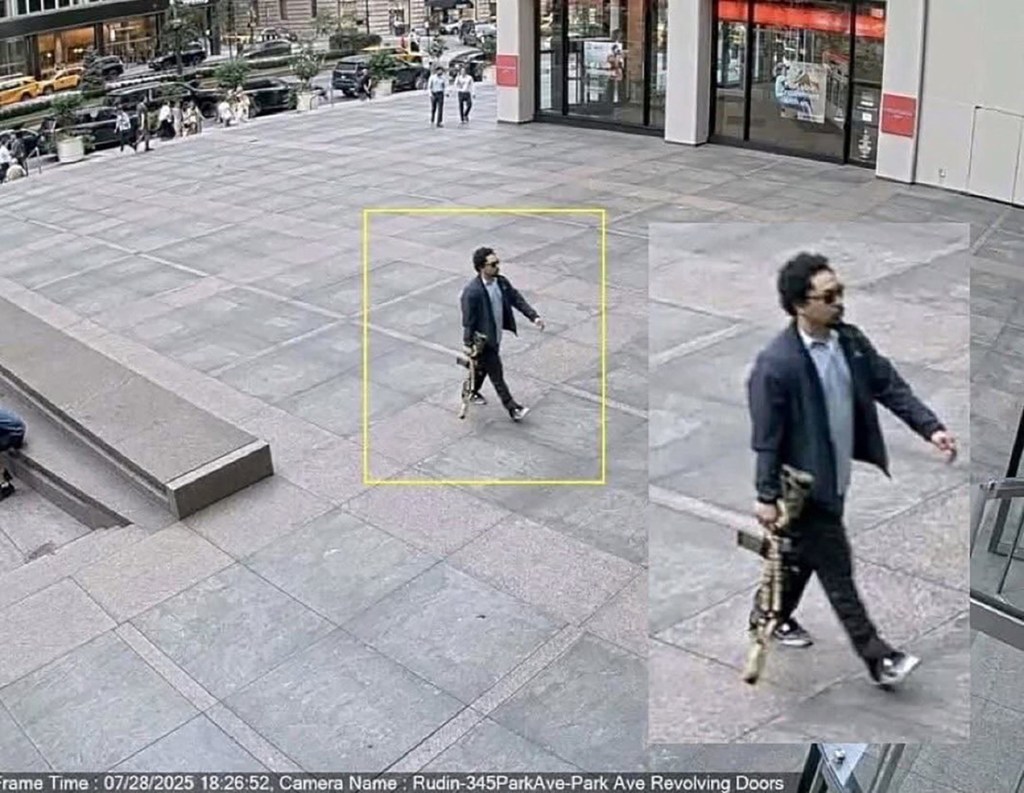 Surveillance image of a man carrying a rifle entering an office building.