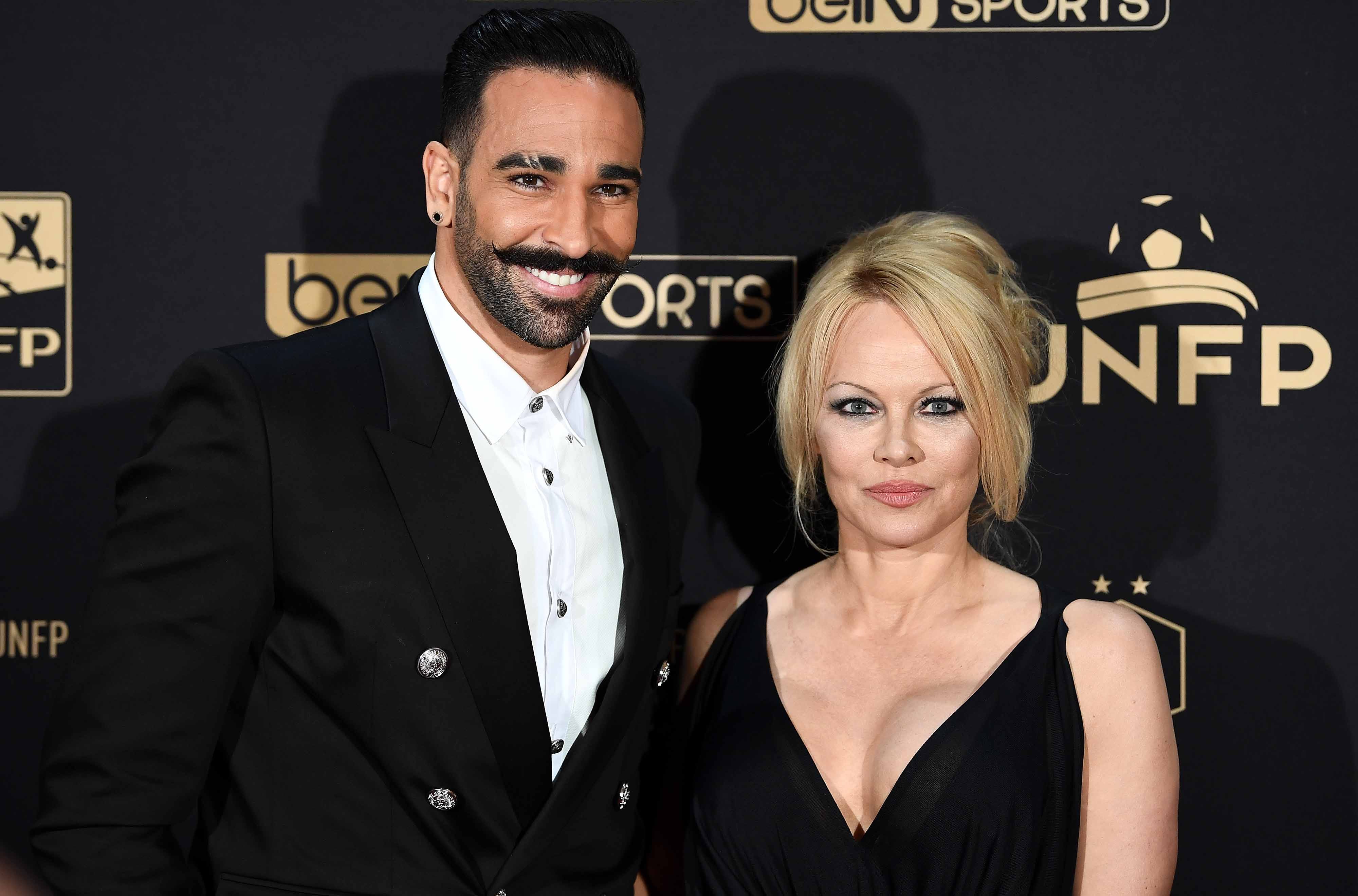Adil Rami in a black suit and white shirt next to Pamela Anderson in a black dress