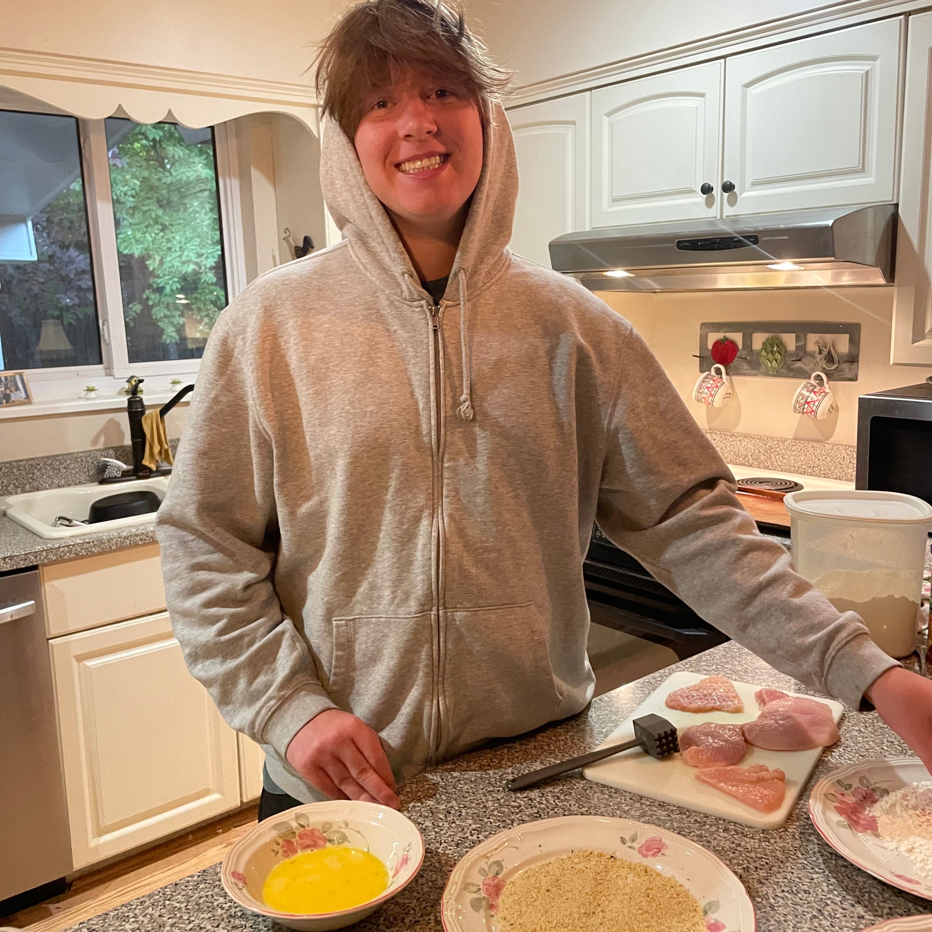 Teenage boy in sweatshirt making chicken cutlets