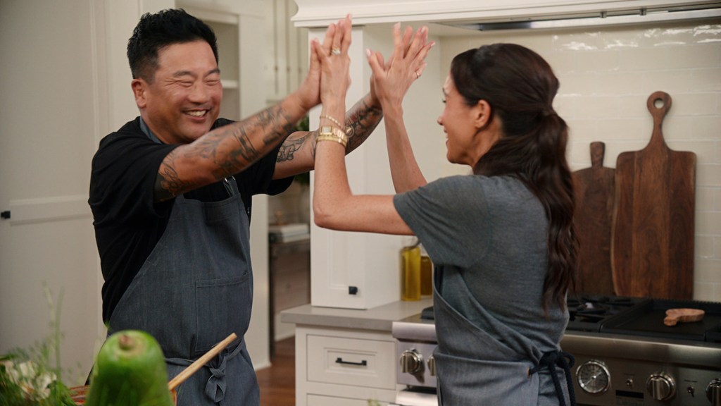  Roy Choi in a black t-shirt and grey apron claps hands with Meghan MArke in a grey apron and grey t-shirt.
