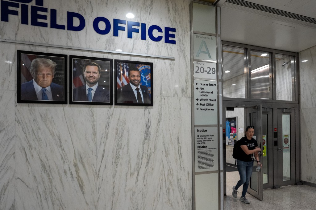 Person exiting an FBI field office in New York City; framed photos of Donald Trump, JD Vance, and Kash Patel are on the wall.