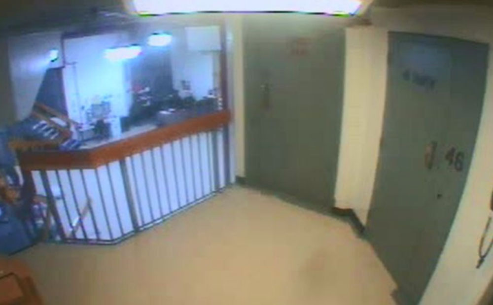 Security camera view of a hallway with a stairwell and a door.