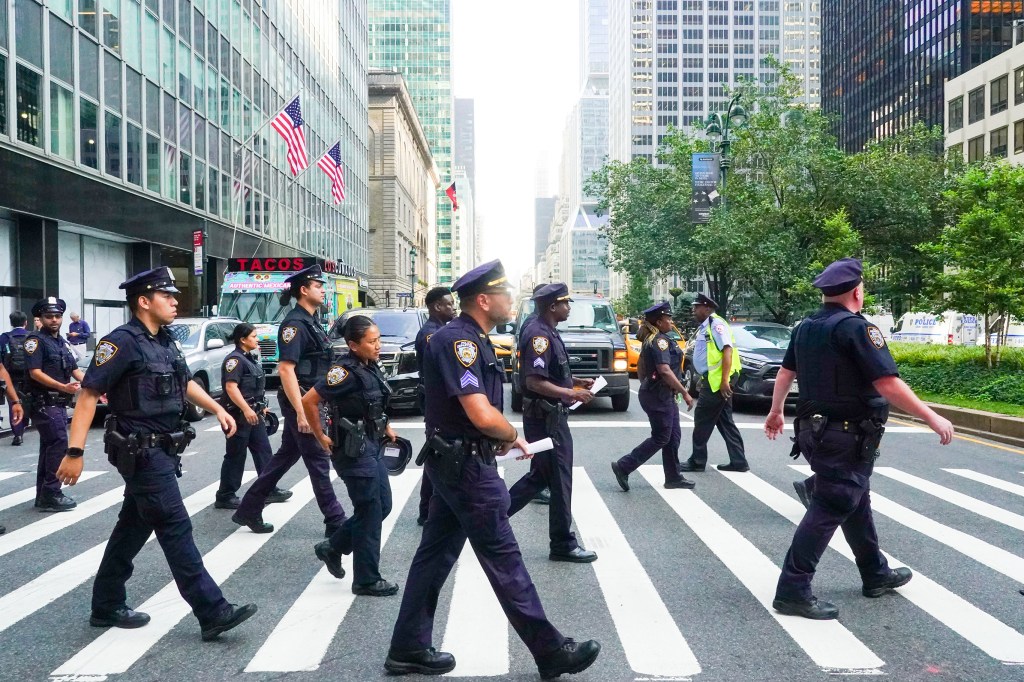 NYPD officers crossing a street near a building following a fatal shooting.