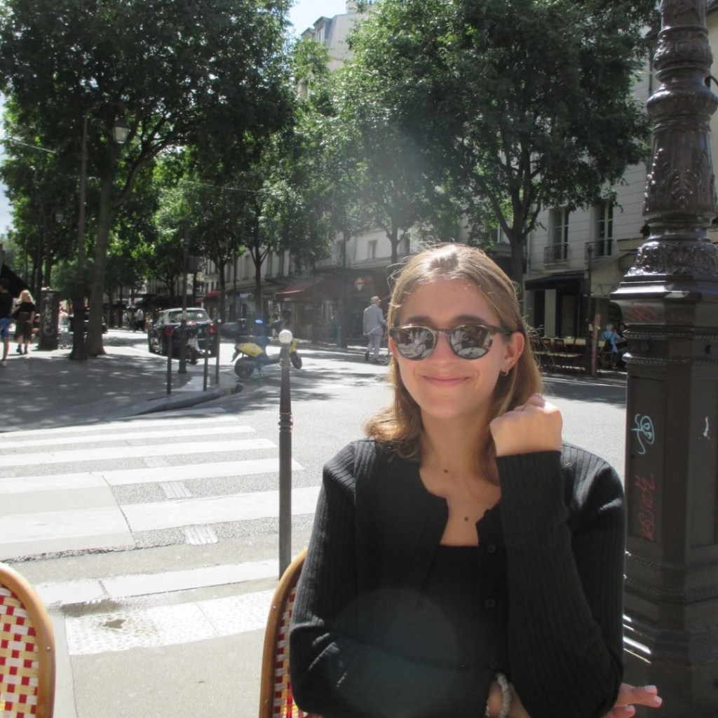 Woman wearing sunglasses, sitting outdoors in Paris.