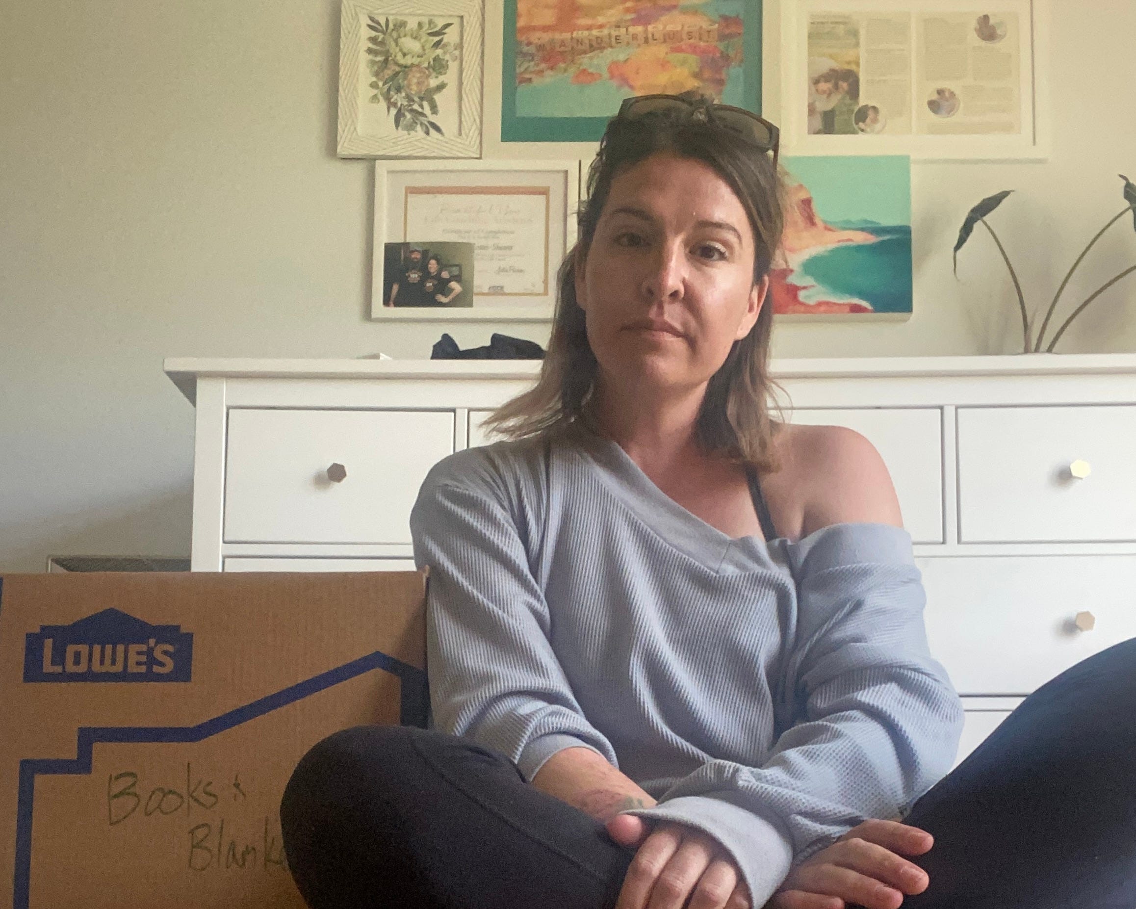 woman sitting on floor looking at camera sitting next to a moving box