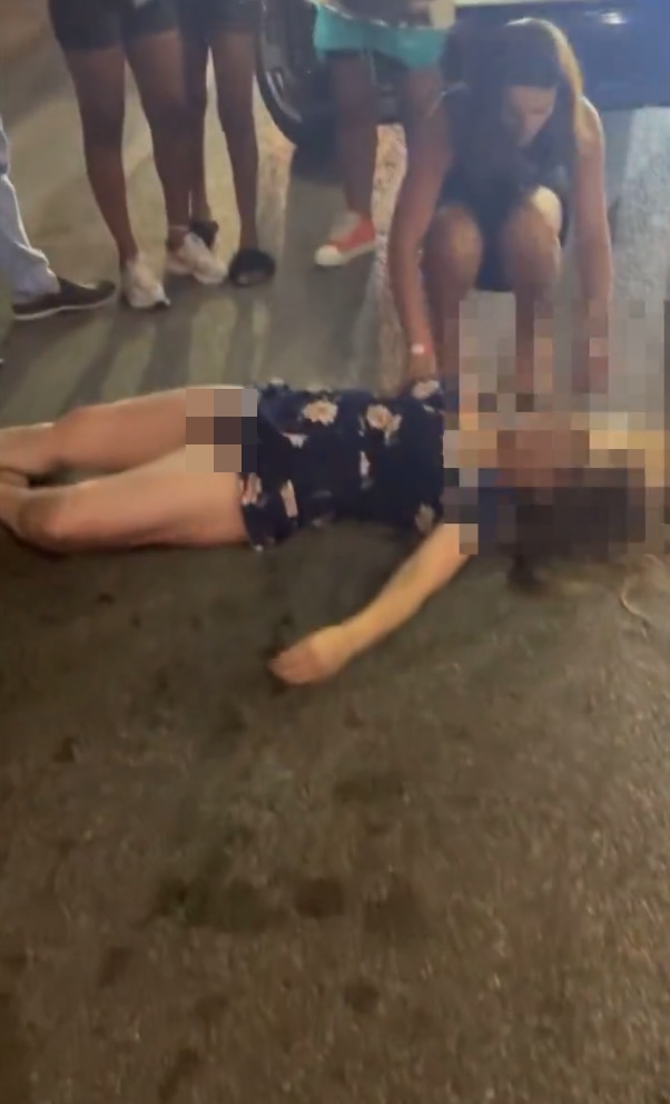 Woman lying unconscious on the ground while others attend to her.