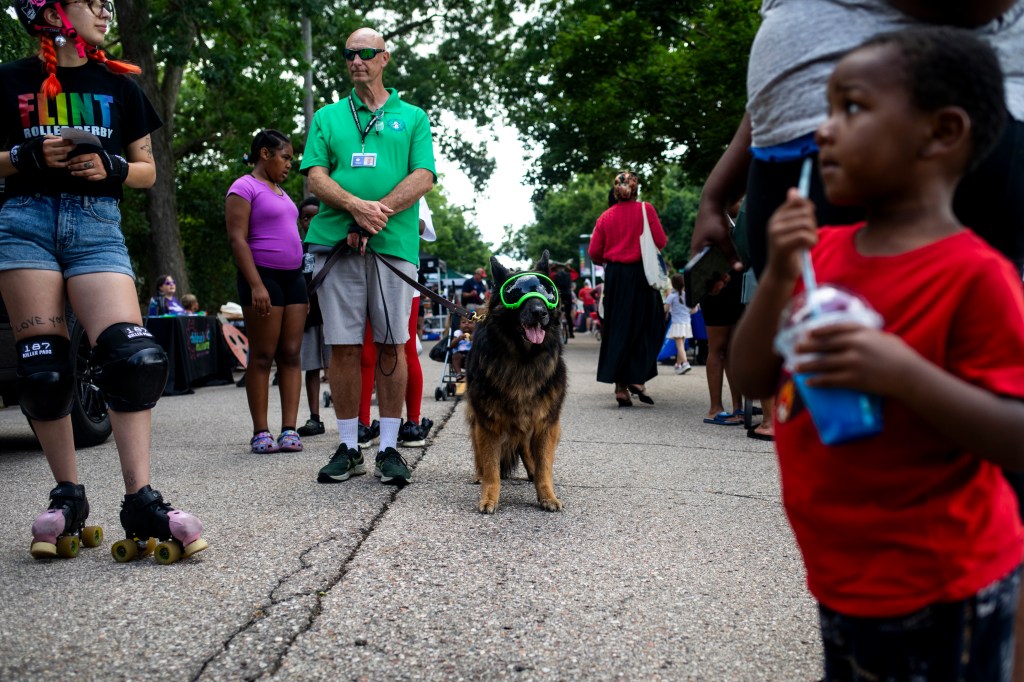 People and a dog wearing goggles wait in line at an outdoor event.