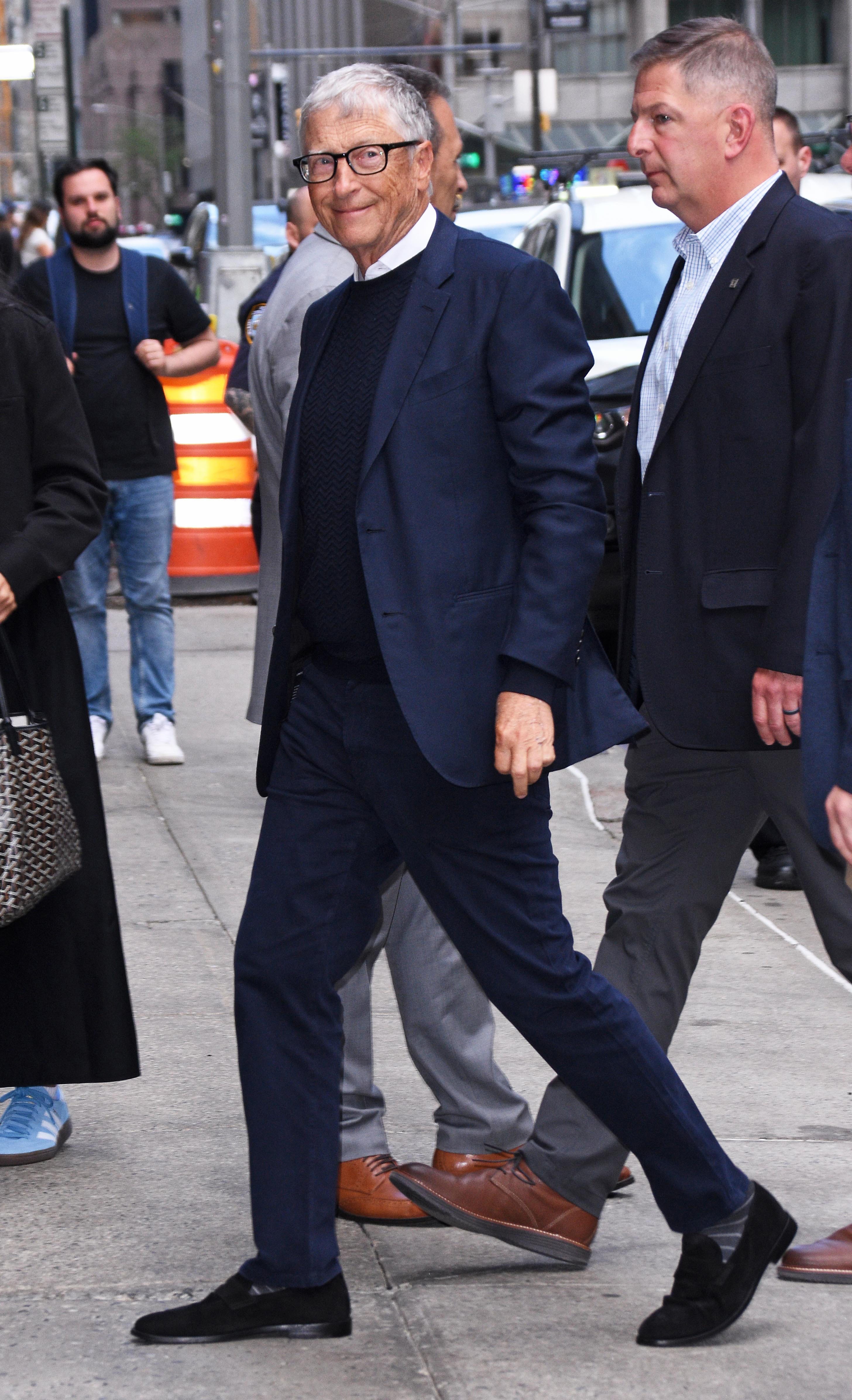 Bill Gates walks in New York City while wearing a navy suit.