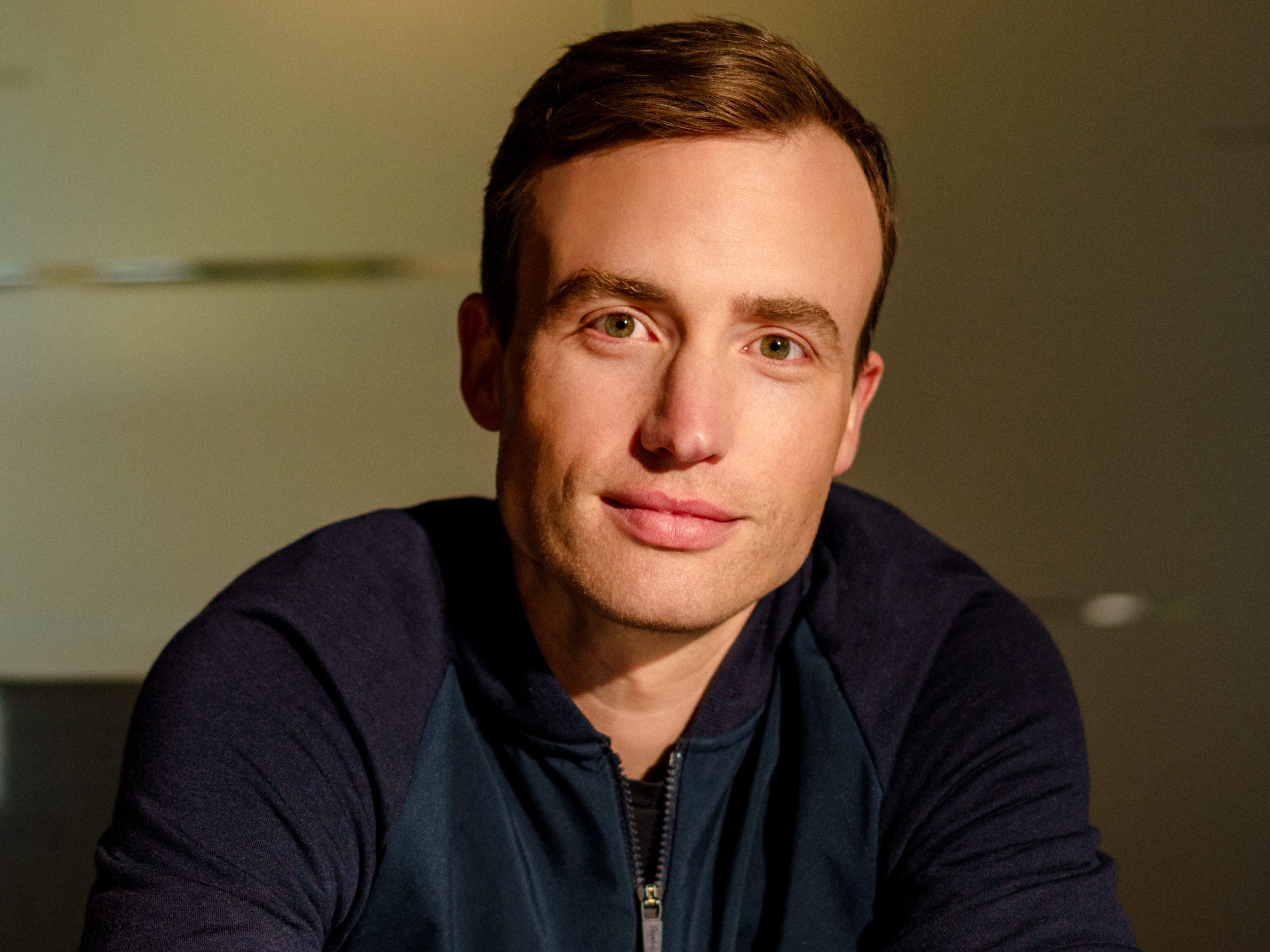 Andrew Reed sitting at a table with his arms crossed, wearing a blue zip-up sweater.