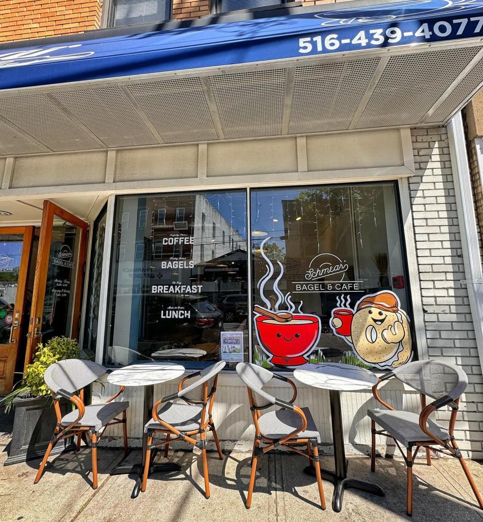 Exterior view of Schmear Bagel & Cafe, showing outdoor seating and a window display featuring illustrations of a bagel and a bowl of soup.