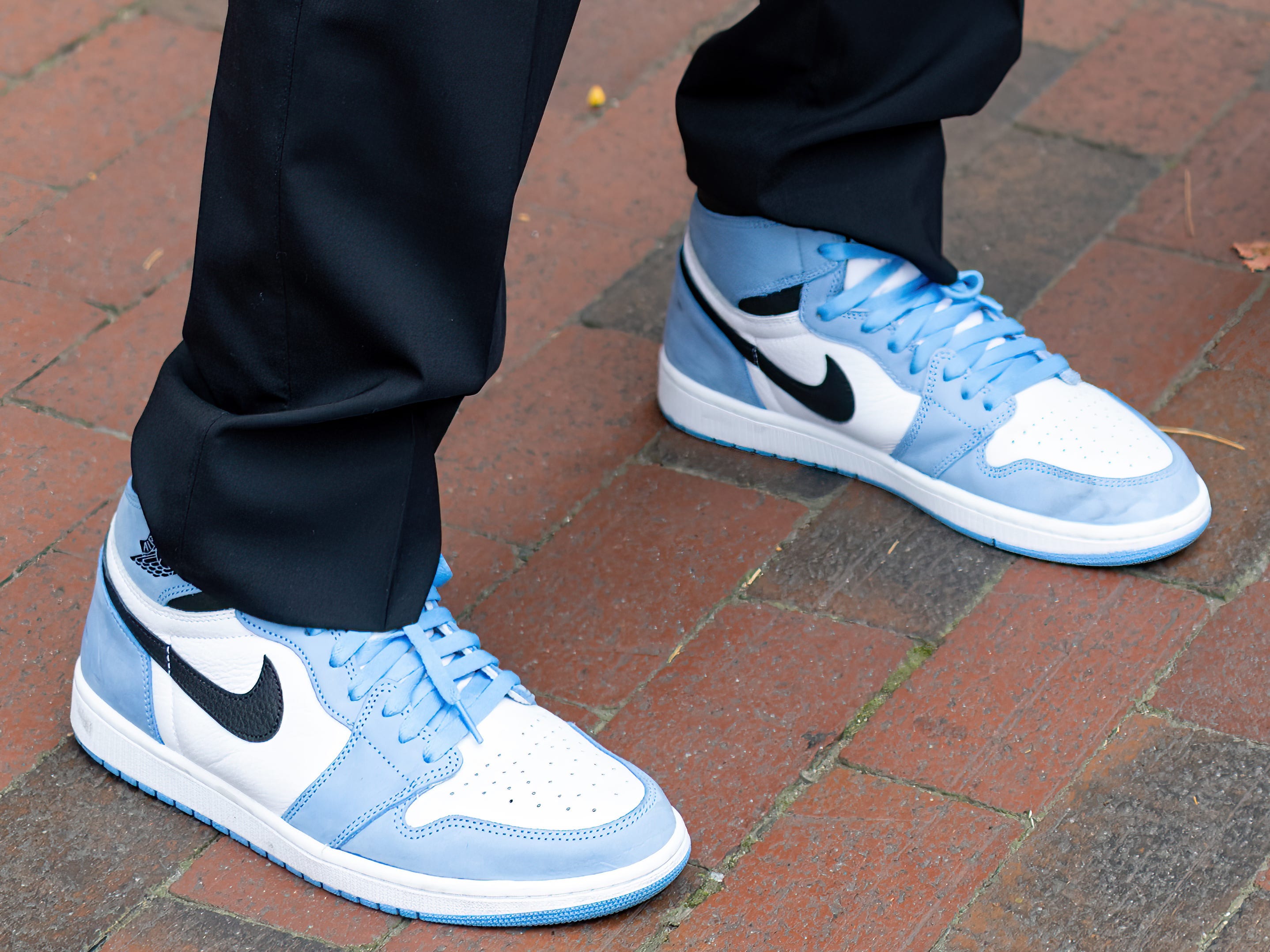 A man wearing black pants and blue, white, and black Nike sneakers.