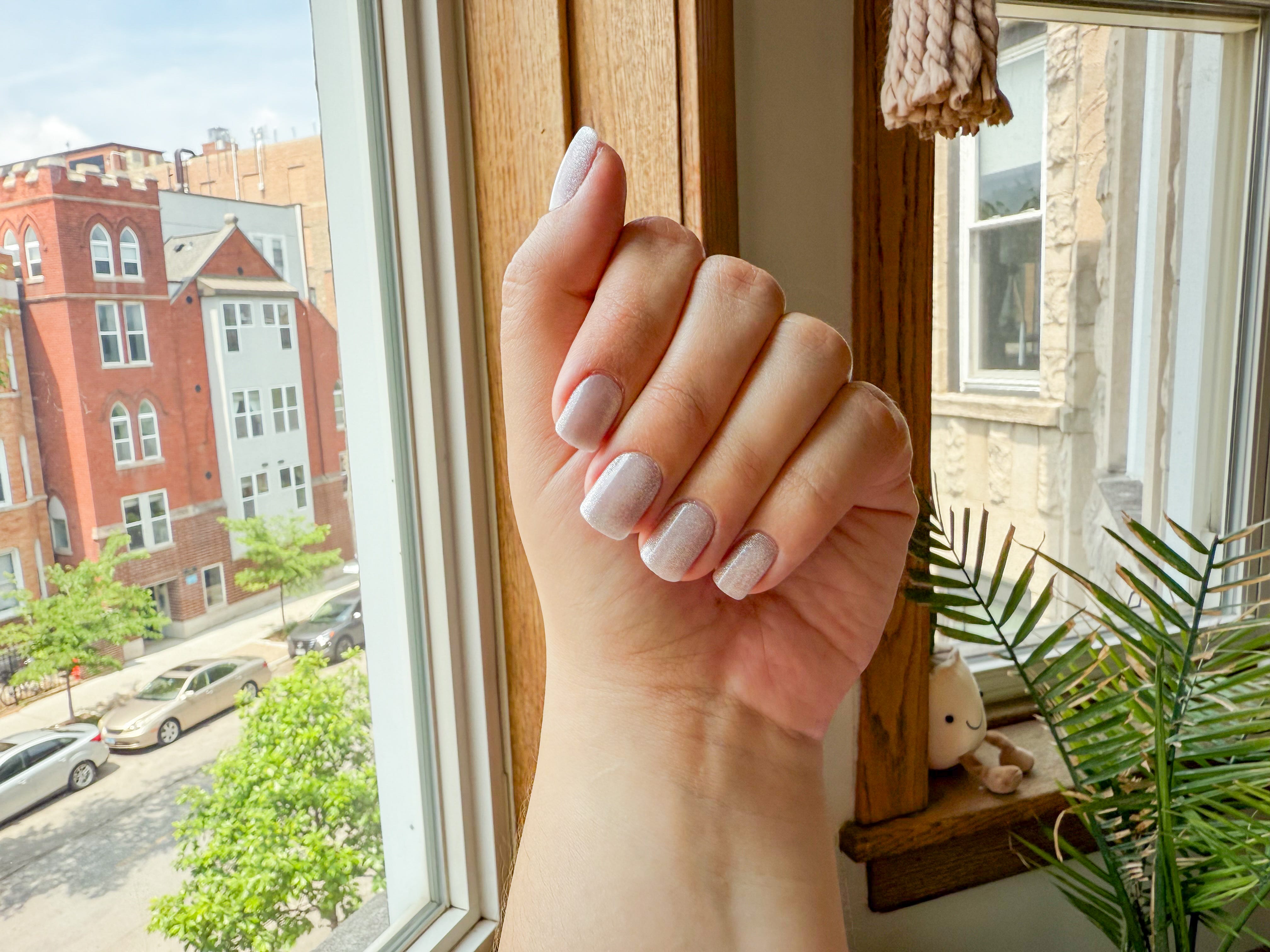 A hand folded downward, displaying a shimmery press-on nail set.